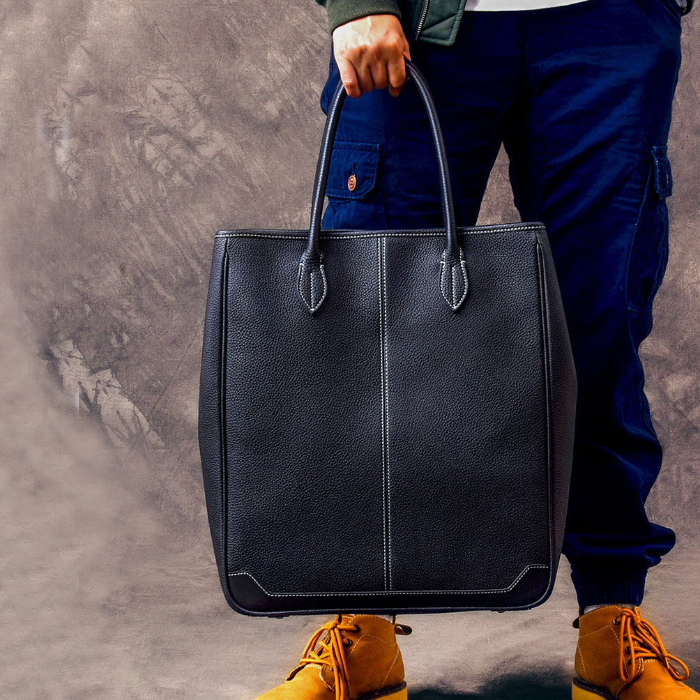 Large vertical cowhide tote bag in black, held by a person, showcasing top-grain leather craftsmanship.
