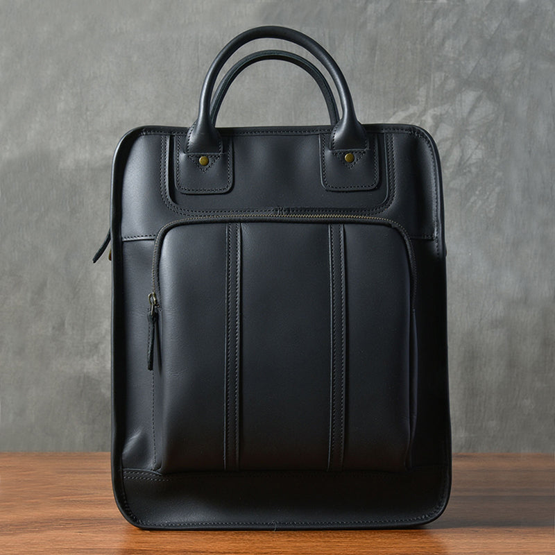 Stylish black leather laptop bag with top handles and front zipper pocket on a wooden surface.