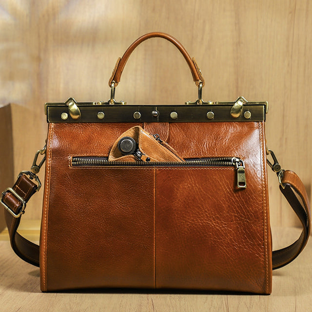 Brown leather crossbody bag with a structured design, featuring a top handle and external zip pocket.