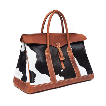 Bag with cow print pattern and brown leather accents on a white background