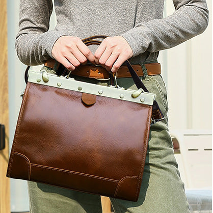 Brown leather crossbody bag with green accents held by a person in casual attire outdoors.