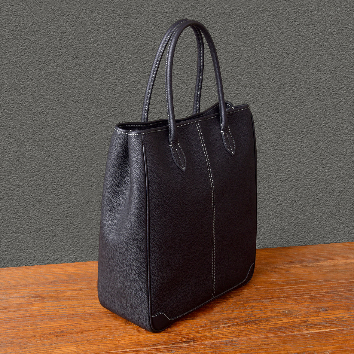 Black large vertical tote bag made of top-grain leather with handles, perfect for laptops and everyday use.