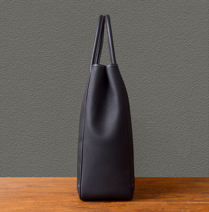 Large vertical cowhide tote bag in black leather, showcasing its sleek side profile on a wooden surface.