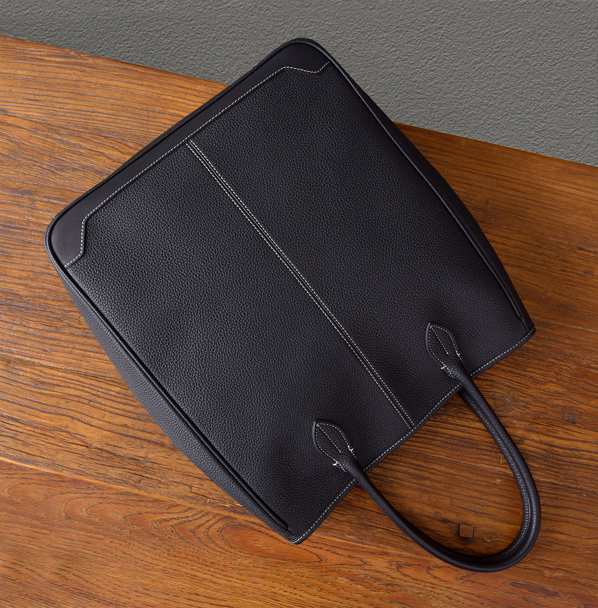 Top view of a large black leather tote bag with elegant stitching on a wooden table.