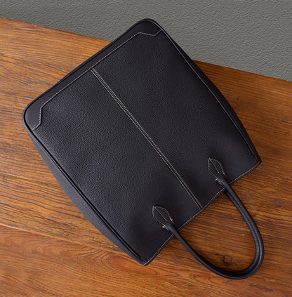 Top view of a large black leather tote bag with elegant stitching on a wooden table.