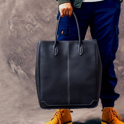 Large vertical cowhide tote bag in black, held by a person, showcasing top-grain leather craftsmanship.