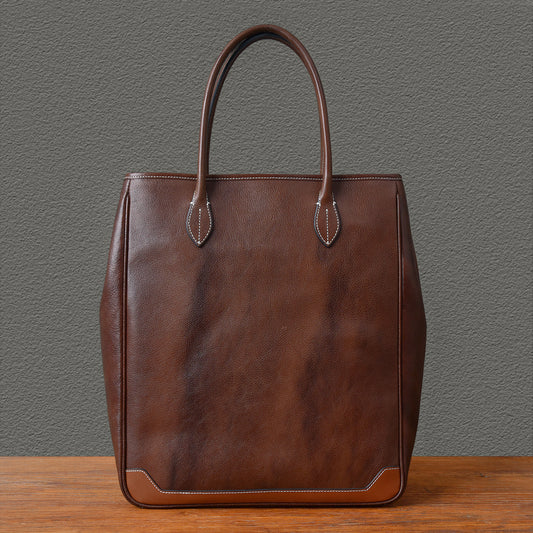 Large vertical brown leather tote bag with sturdy handles and minimalist design.