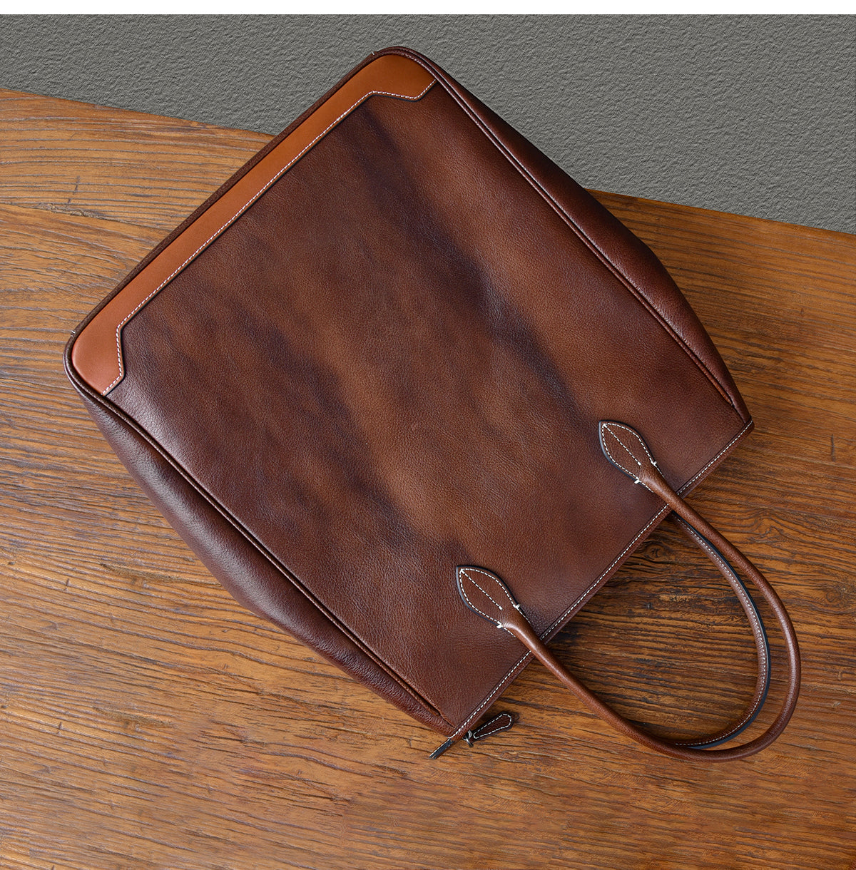 Large vertical brown cowhide tote bag with top-grain leather, viewed from above on a wooden surface.