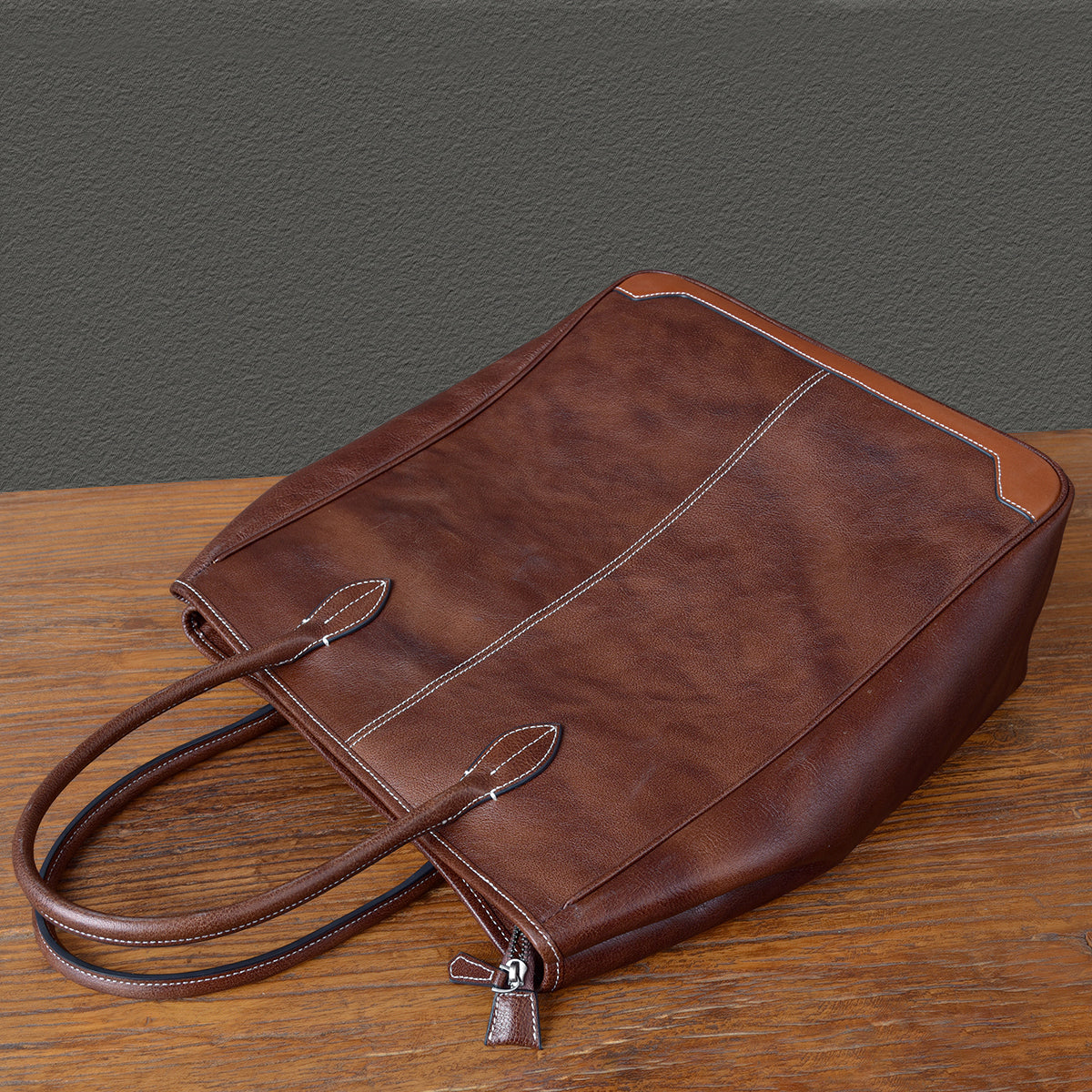 Large brown vertical cowhide tote bag with leather straps, handcrafted from top-grain leather, stylish unisex design.