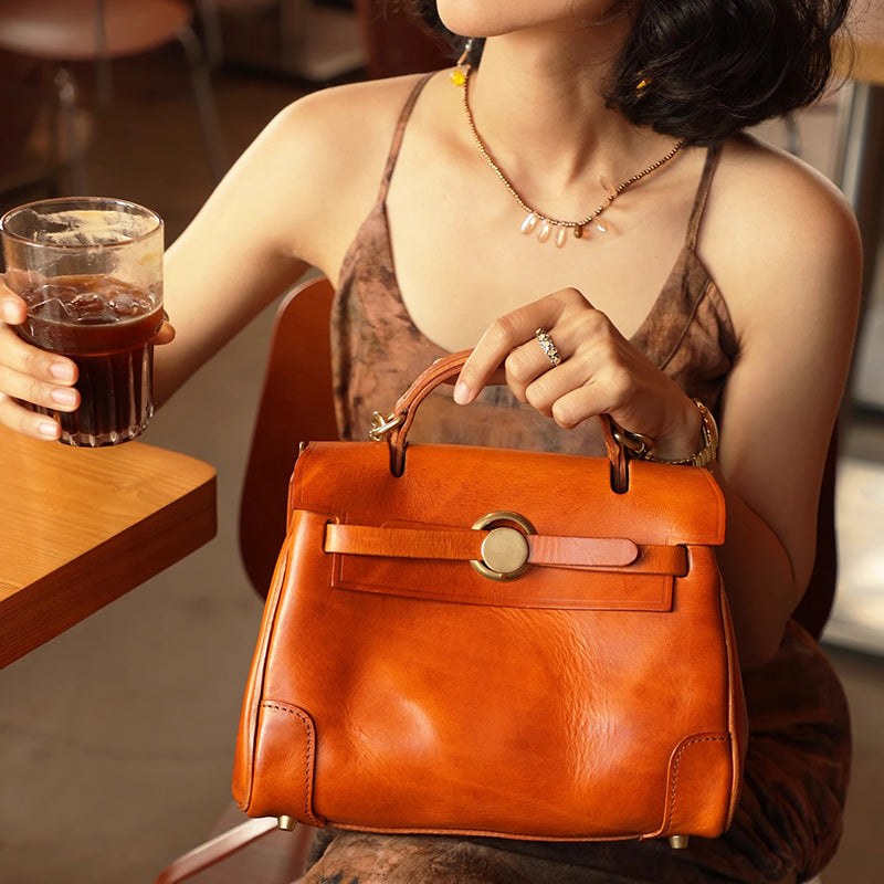 Classic Leather Bag in orange, held by woman with a drink, showcasing its stylish design and elegant craftsmanship.