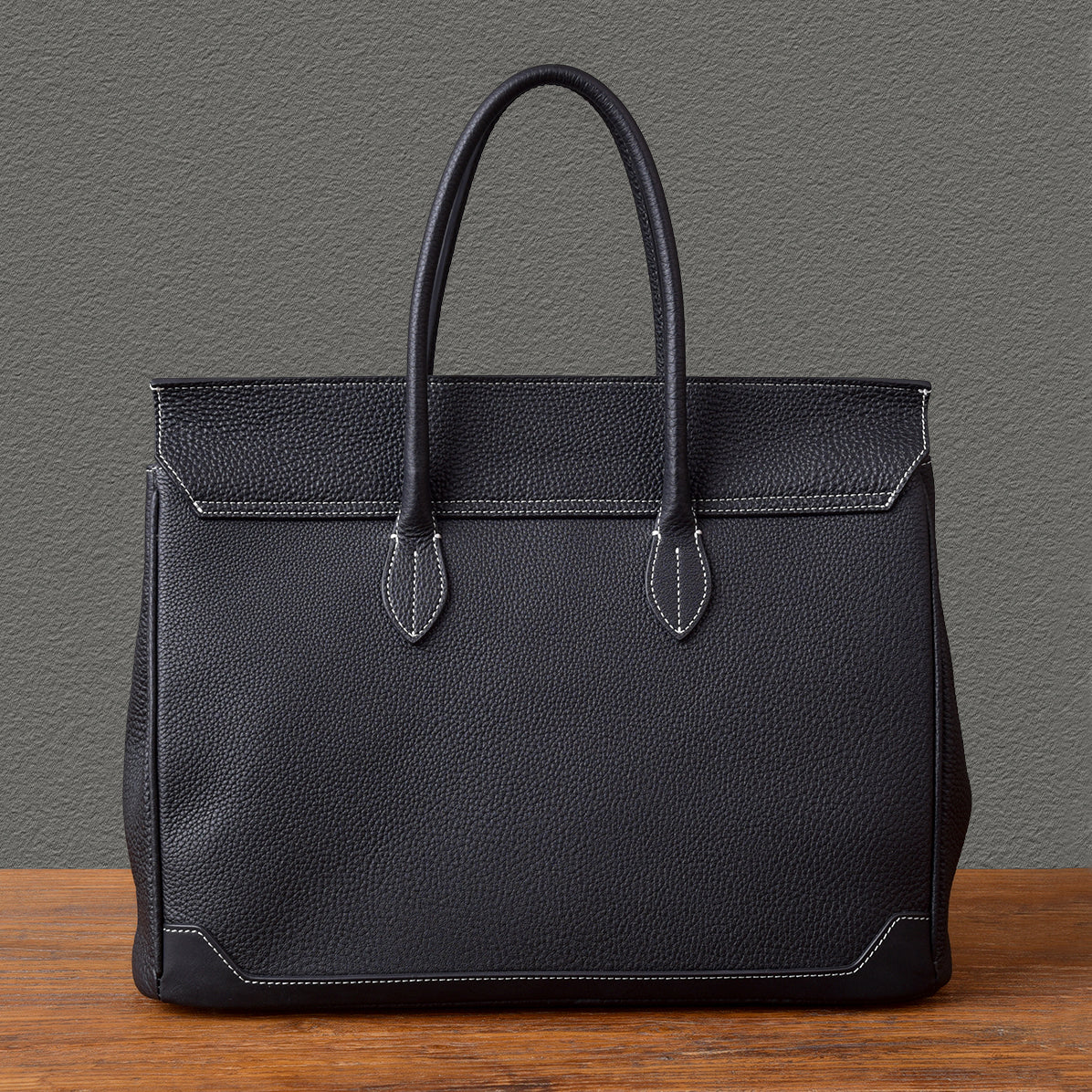 Black leather work tote bag with sturdy handles on a wooden table.