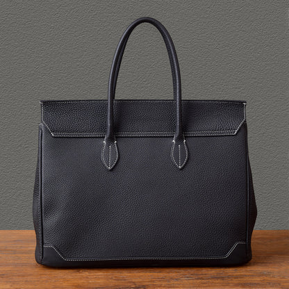 Black leather work tote bag with sturdy handles on a wooden table.