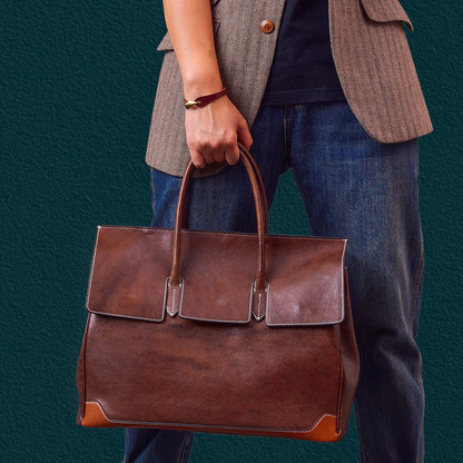 Person holding a top-grain leather large business tote bag in brown, suitable for laptops and business use.