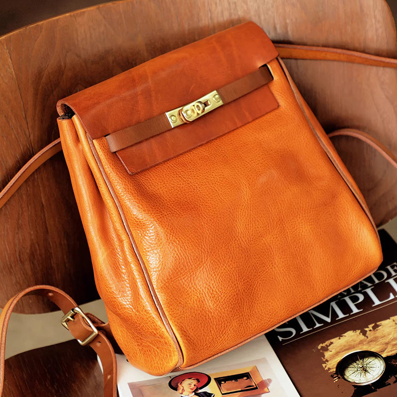 Vegetable tanned leather backpack women small rucksack in rich orange color on a wooden table with magazines.