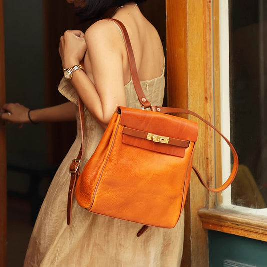 Leather Backpack Women in orange, stylish small rucksack worn over shoulder by woman in dress.