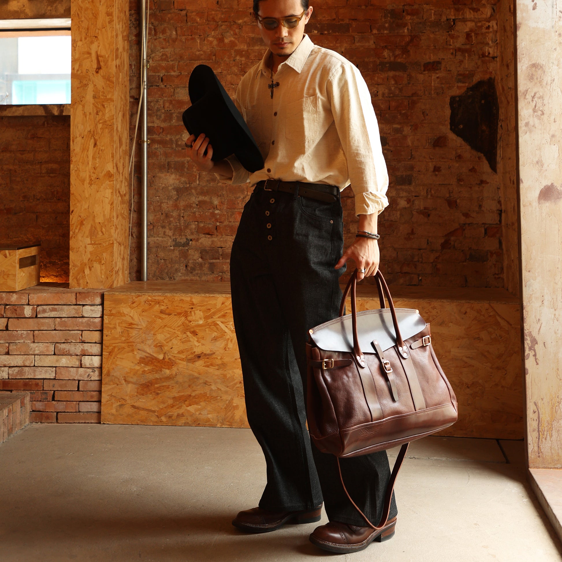 Man in stylish outfit holding a hat and Italian Leather Travel Bag, showcasing the bag's elegance and functionality.