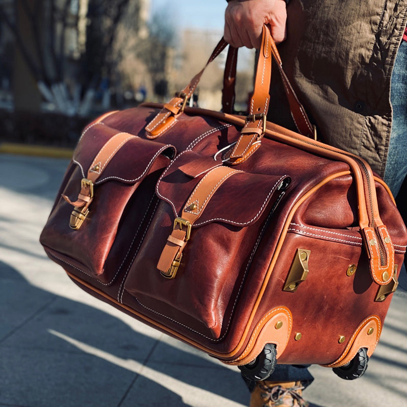 Handmade Leather Travel Bag With Wheels, 23.6in carry on rolling duffel luggage being held outdoors.
